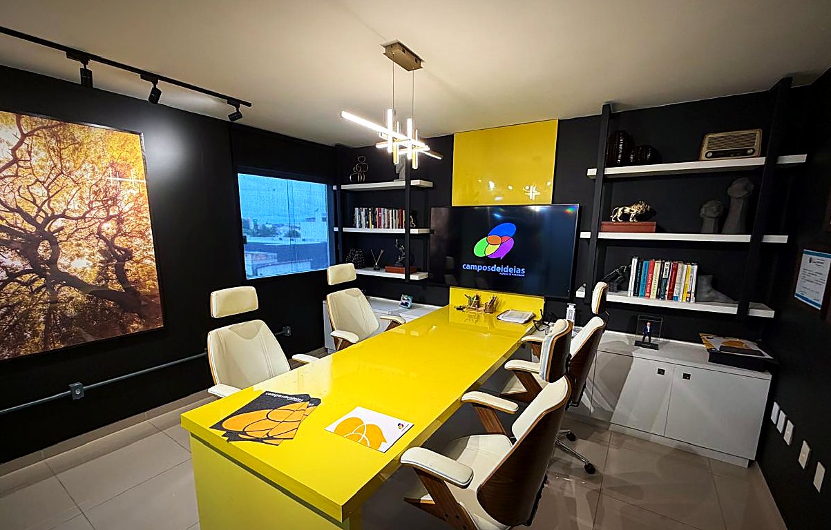 Sala de reunião da Campos de Ideias com mesa amarela, paredes pretas e estantes de livros
